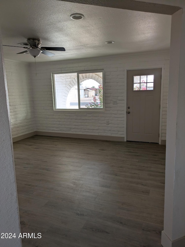 foyer entrance with a textured ceiling, dark hardwood / wood-style floors, ceiling fan, and brick wall