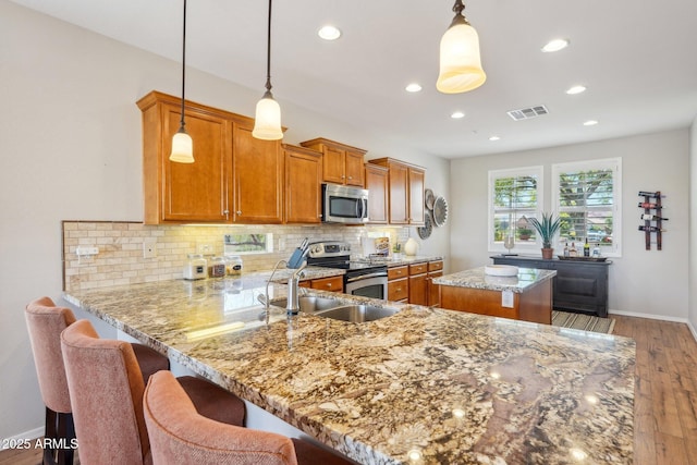 28351 N 130th Dr, Peoria, AZ 85383 - kitchen featuring stainless steel appliances, brown cabinetry, a center island, light wood finished floors, and backsplash