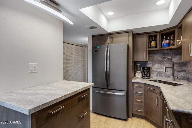 kitchen with a sink, visible vents, dark brown cabinets, freestanding refrigerator, and light wood finished floors