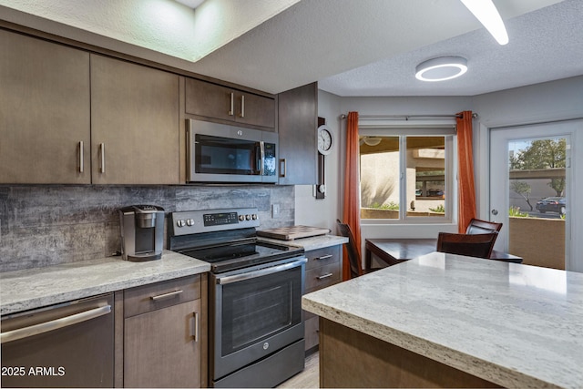 kitchen with a textured ceiling, dark brown cabinets, appliances with stainless steel finishes, and decorative backsplash