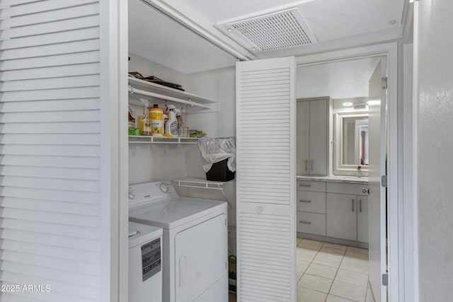 clothes washing area featuring washer and clothes dryer, light tile patterned floors, visible vents, a sink, and laundry area