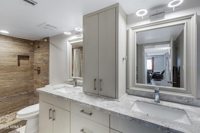 full bath featuring tiled shower, a sink, toilet, and double vanity