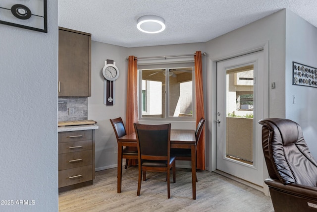 dining area with light wood finished floors, baseboards, and a textured ceiling