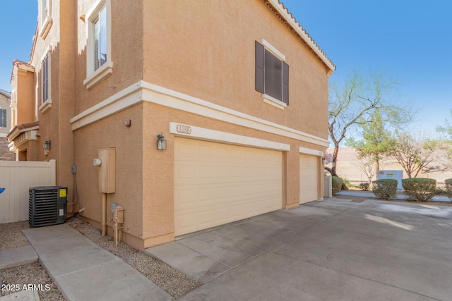 view of side of property with stucco siding, concrete driveway, an attached garage, cooling unit, and a tiled roof