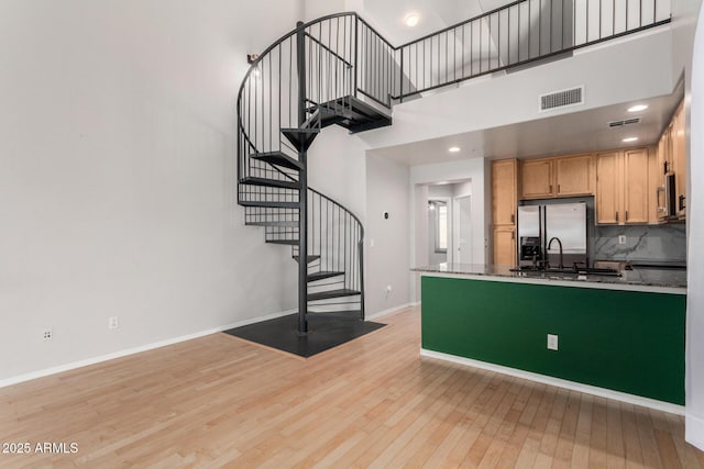 kitchen with a towering ceiling, visible vents, baseboards, light wood-type flooring, and stainless steel refrigerator with ice dispenser