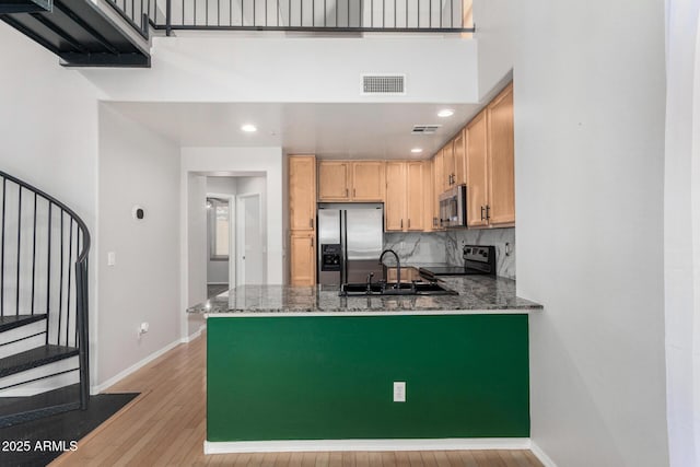 kitchen featuring stainless steel appliances, visible vents, a sink, dark stone countertops, and a peninsula