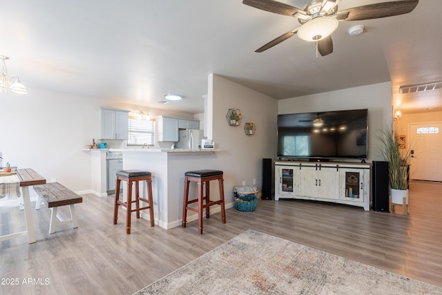 living area with baseboards, ceiling fan with notable chandelier, wood finished floors, and visible vents
