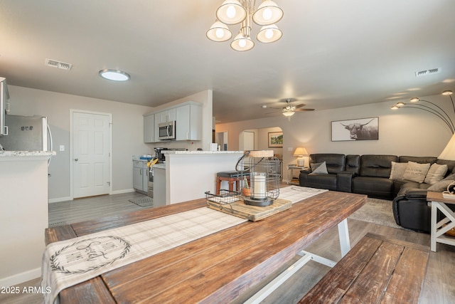 dining room featuring baseboards, visible vents, wood finished floors, and ceiling fan with notable chandelier
