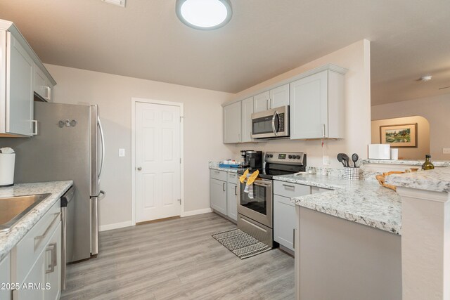 kitchen with light stone countertops, appliances with stainless steel finishes, light wood-style floors, a peninsula, and gray cabinetry