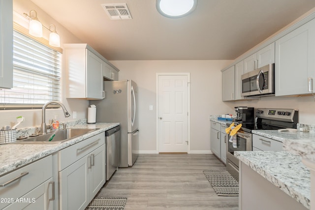 kitchen featuring a sink, light wood-style flooring, stainless steel appliances, baseboards, and visible vents