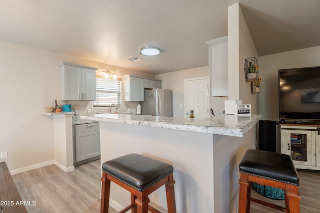 kitchen featuring freestanding refrigerator, light wood finished floors, a breakfast bar area, and wine cooler