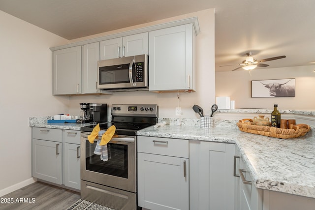 kitchen with ceiling fan, baseboards, a peninsula, stainless steel appliances, and light wood-style flooring