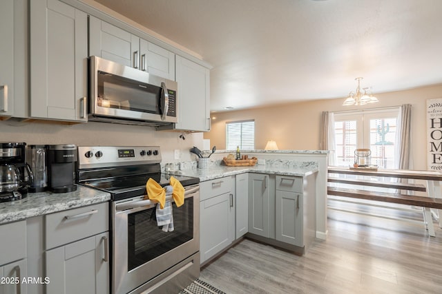 kitchen featuring appliances with stainless steel finishes, gray cabinetry, a peninsula, an inviting chandelier, and light wood-style flooring