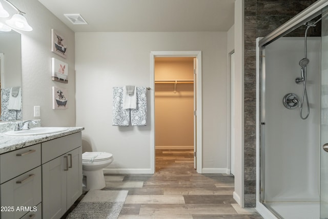 full bath with a walk in closet, vanity, a shower stall, wood finished floors, and visible vents