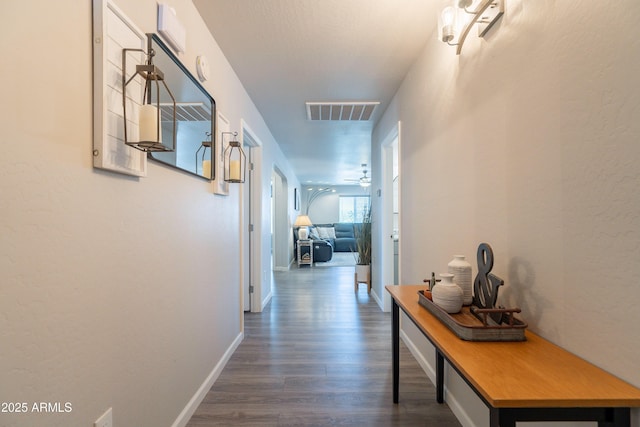 hall with visible vents, baseboards, and dark wood-type flooring
