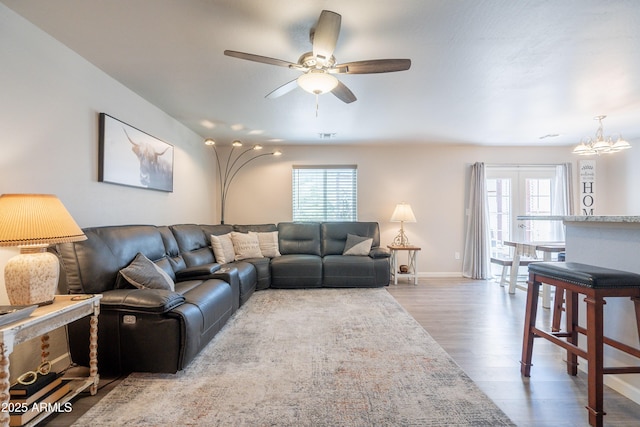 living room featuring plenty of natural light, baseboards, ceiling fan with notable chandelier, and wood finished floors