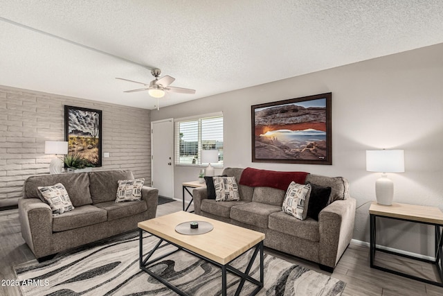 living room with ceiling fan, brick wall, hardwood / wood-style floors, and a textured ceiling