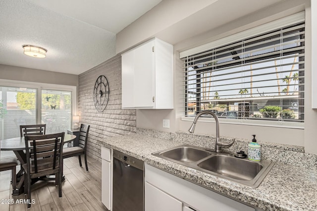 kitchen with sink, dishwasher, white cabinetry, light hardwood / wood-style floors, and a textured ceiling