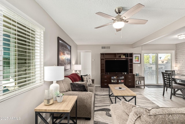 living room featuring ceiling fan, a textured ceiling, and light wood-type flooring