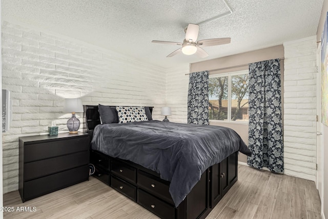 bedroom featuring ceiling fan, brick wall, a textured ceiling, and light wood-type flooring