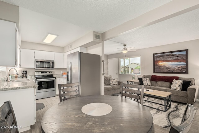 dining area featuring ceiling fan, sink, light hardwood / wood-style flooring, and a textured ceiling