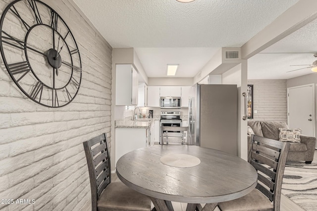 dining room featuring sink, a textured ceiling, ceiling fan, and brick wall