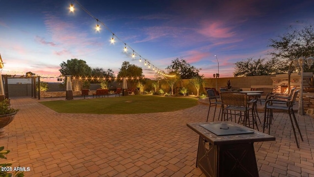 patio terrace at dusk with a yard and an outdoor stone fireplace