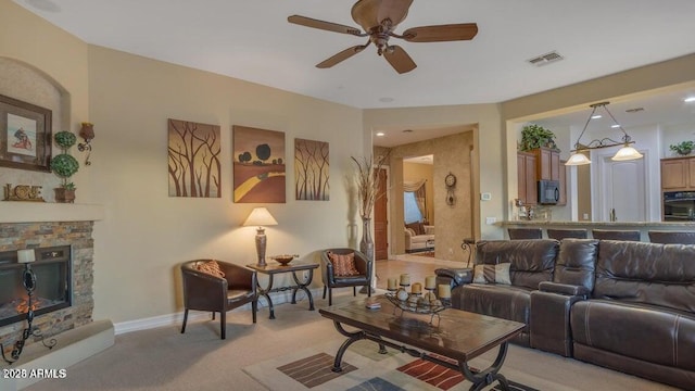 living room featuring a stone fireplace, light colored carpet, and ceiling fan