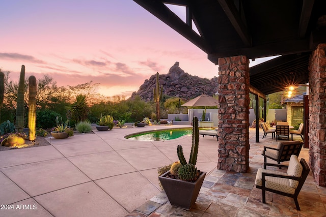 patio terrace at dusk with a fenced in pool and a mountain view