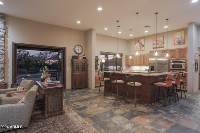 kitchen featuring a high ceiling, a breakfast bar area, decorative light fixtures, light stone counters, and stainless steel appliances