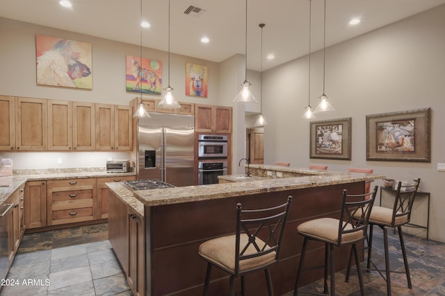 kitchen featuring a breakfast bar, a kitchen island with sink, hanging light fixtures, light stone countertops, and appliances with stainless steel finishes