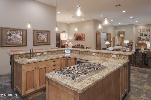 kitchen with light stone countertops, decorative light fixtures, stainless steel gas stovetop, and sink