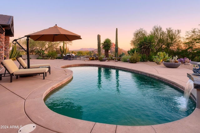 pool at dusk with pool water feature and a patio area