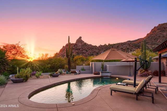 pool at dusk with pool water feature, a mountain view, and a patio area