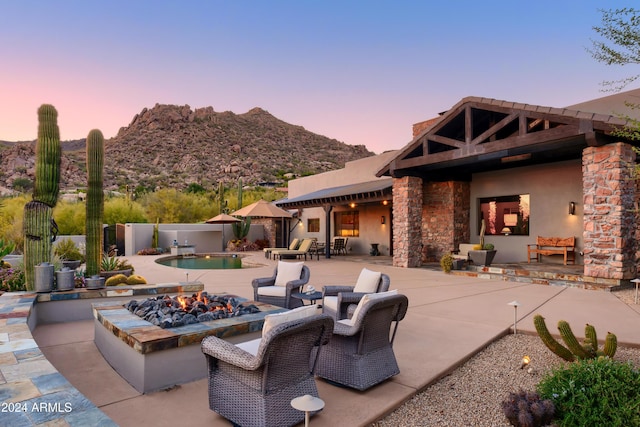 patio terrace at dusk with a fenced in pool, a mountain view, and a fire pit