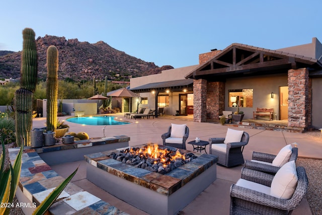 pool at dusk featuring a fire pit, a mountain view, a patio, and exterior fireplace