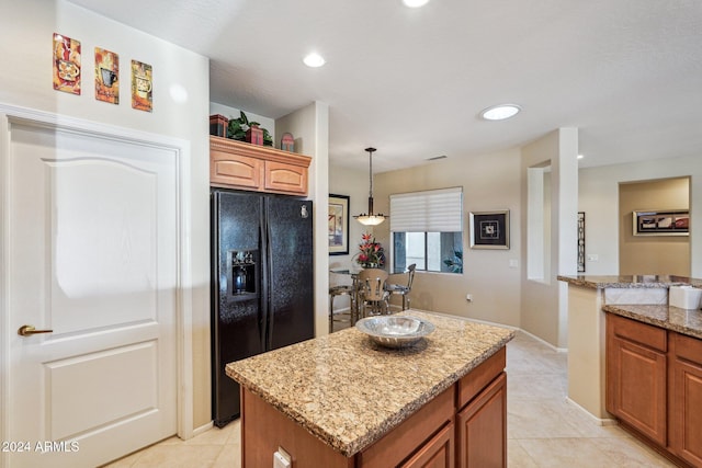 kitchen with pendant lighting, a center island, black fridge, and light stone countertops