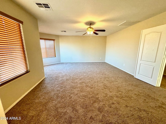 spare room featuring ceiling fan, dark carpet, and a textured ceiling