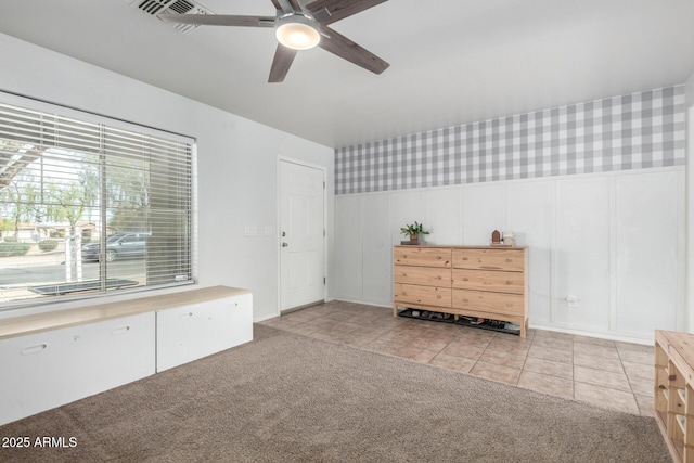 interior space featuring wallpapered walls, ceiling fan, a wainscoted wall, light colored carpet, and light tile patterned floors