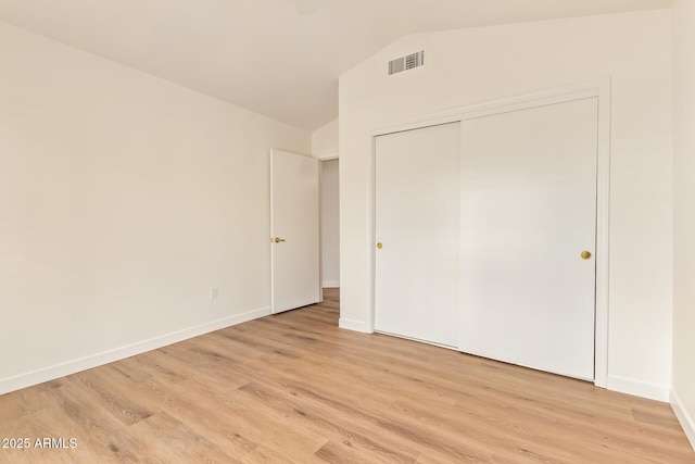 unfurnished bedroom with visible vents, a closet, baseboards, light wood finished floors, and vaulted ceiling