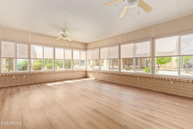 unfurnished sunroom featuring brick wall, plenty of natural light, and wood finished floors