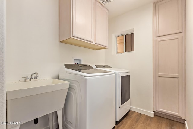 laundry area featuring washer and dryer, cabinet space, a sink, baseboards, and light wood-type flooring