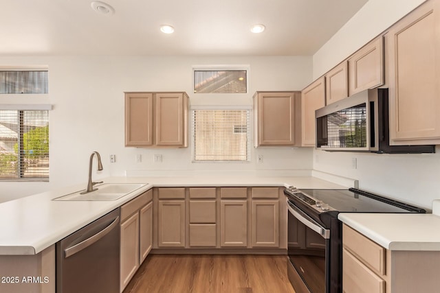 kitchen with appliances with stainless steel finishes, a sink, light countertops, a peninsula, and light wood-type flooring