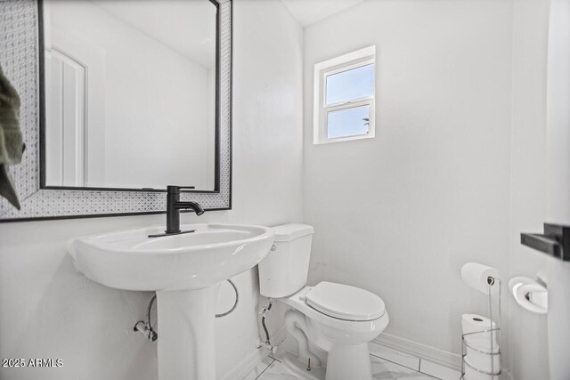 half bath featuring marble finish floor, toilet, and baseboards