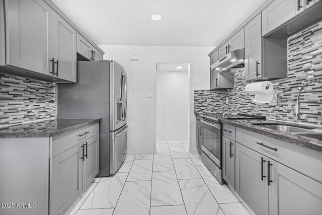 kitchen featuring dark stone counters, a sink, stainless steel appliances, under cabinet range hood, and marble finish floor