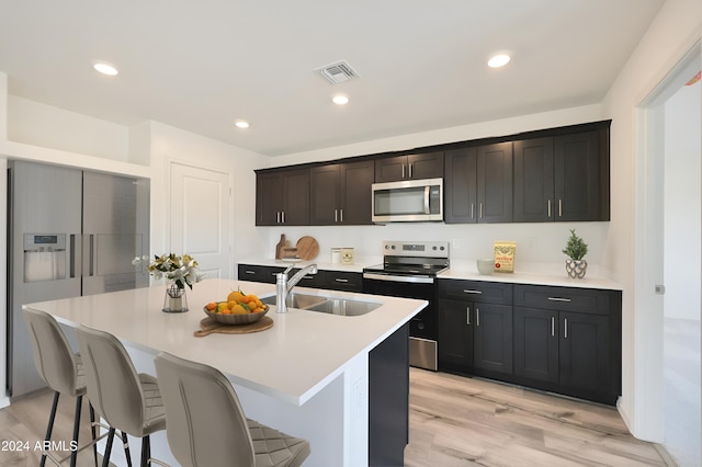 kitchen with sink, light hardwood / wood-style flooring, a kitchen island with sink, a breakfast bar, and appliances with stainless steel finishes