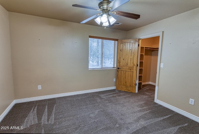 unfurnished bedroom featuring dark carpet, a closet, a spacious closet, and ceiling fan