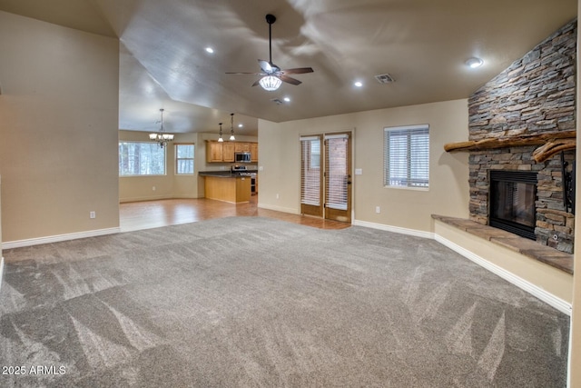 unfurnished living room with ceiling fan with notable chandelier, light colored carpet, a stone fireplace, and lofted ceiling