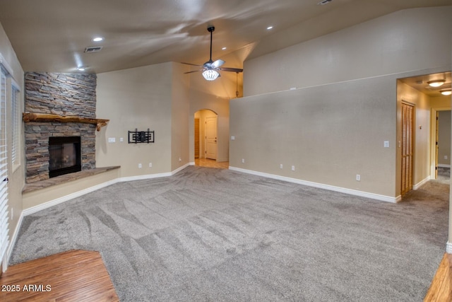 unfurnished living room with carpet, ceiling fan, a stone fireplace, and high vaulted ceiling