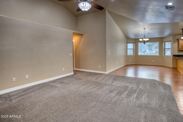 carpeted spare room featuring ceiling fan with notable chandelier and vaulted ceiling